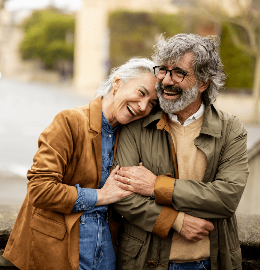 Elderly couple smiling and embracing outdoors.