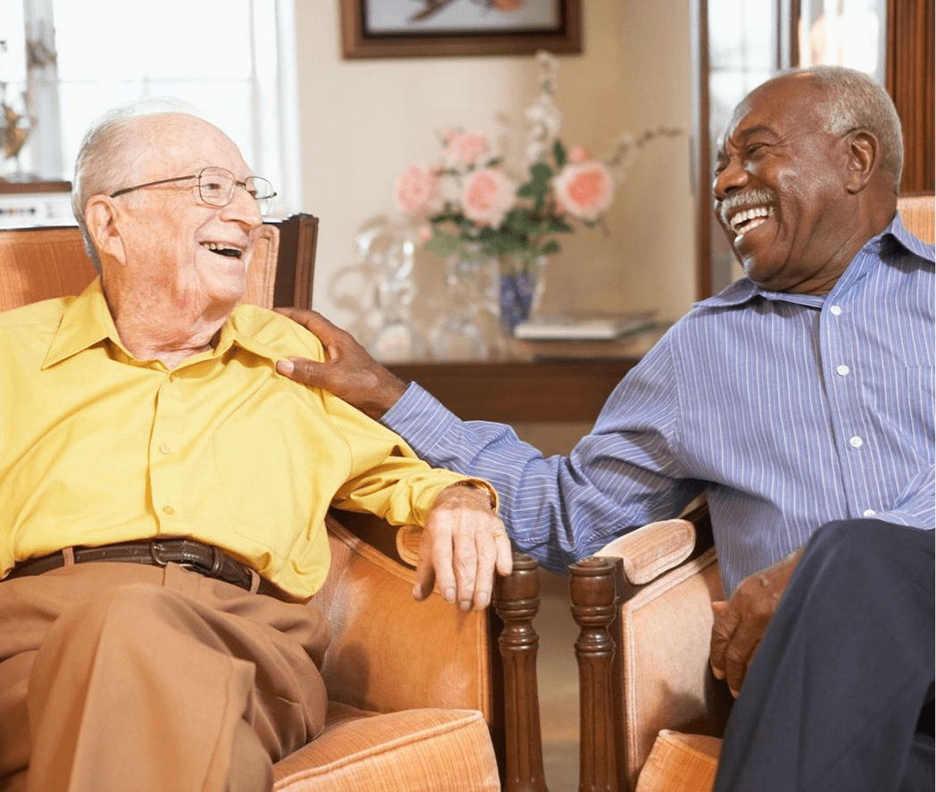 Two elderly men laughing together at home.